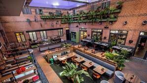 A spacious indoor area with multiple seating arrangements, including tables and benches, surrounded by potted plants and a brick wall. - Comfort Hotel Vesterbro (Copenhagen)