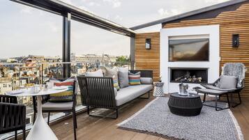 A modern balcony with a sofa, chairs, and a table, overlooking a cityscape.