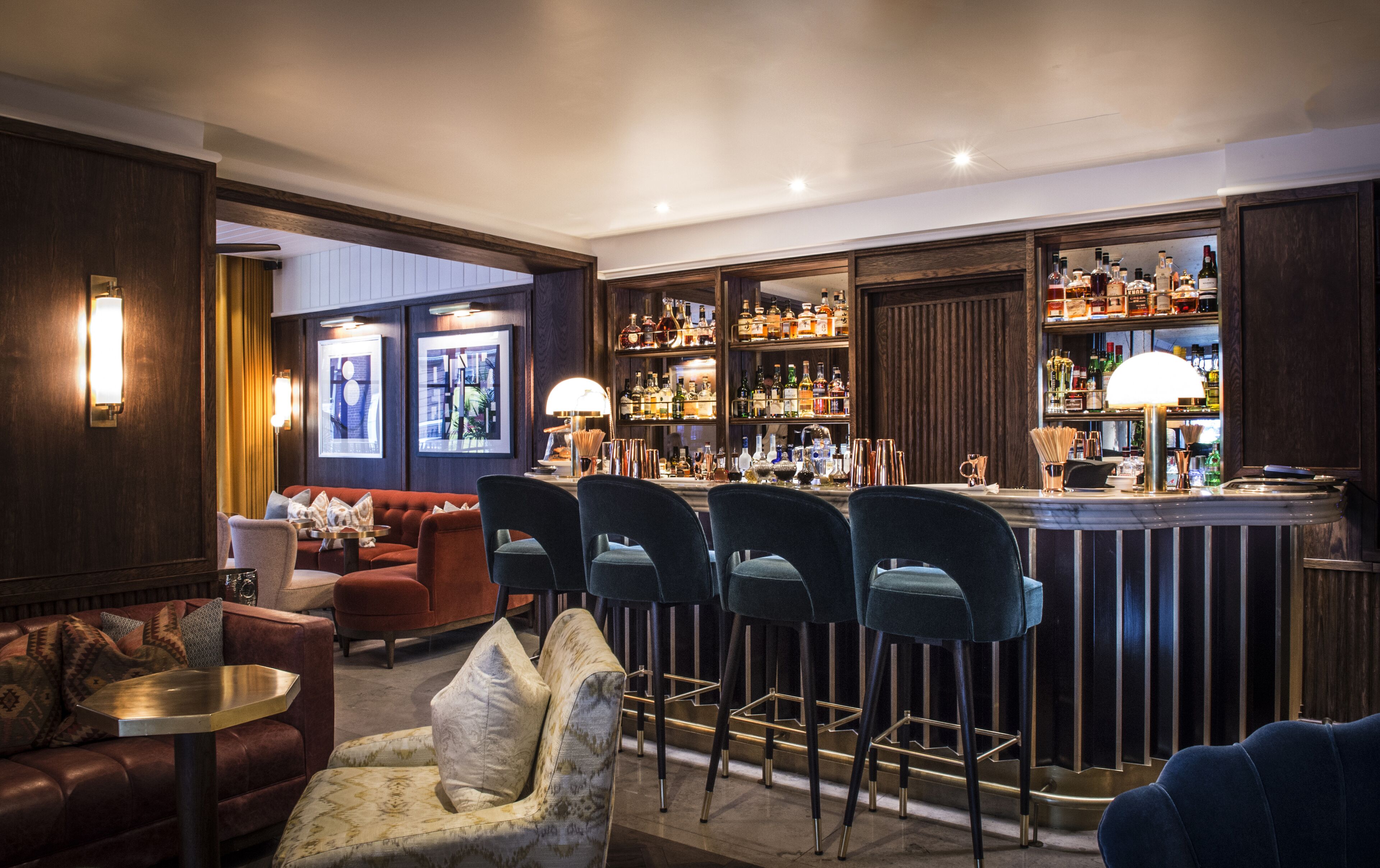 A bar area with multiple seating options, including bar stools and a sofa. There are shelves with various bottles and glasses.