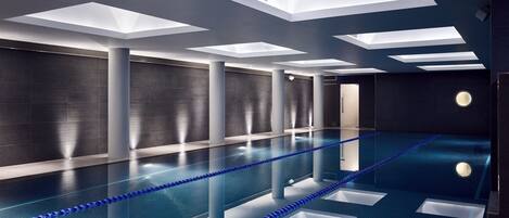 A modern indoor pool with clear water, blue lane dividers, and geometric ceiling skylights.
