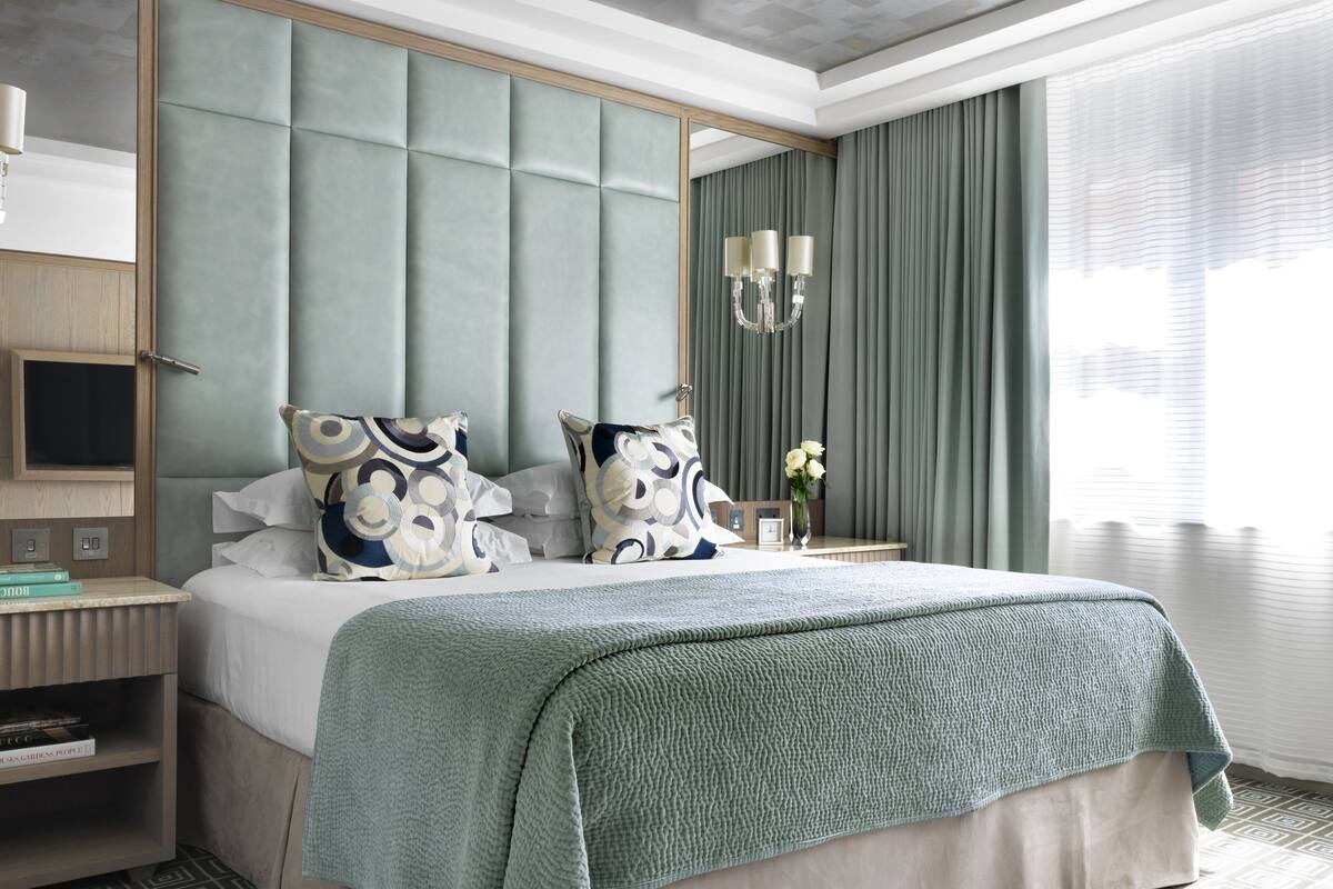 A modern hotel room with a large bed, a nightstand, a bedside table, and a large window with curtains.