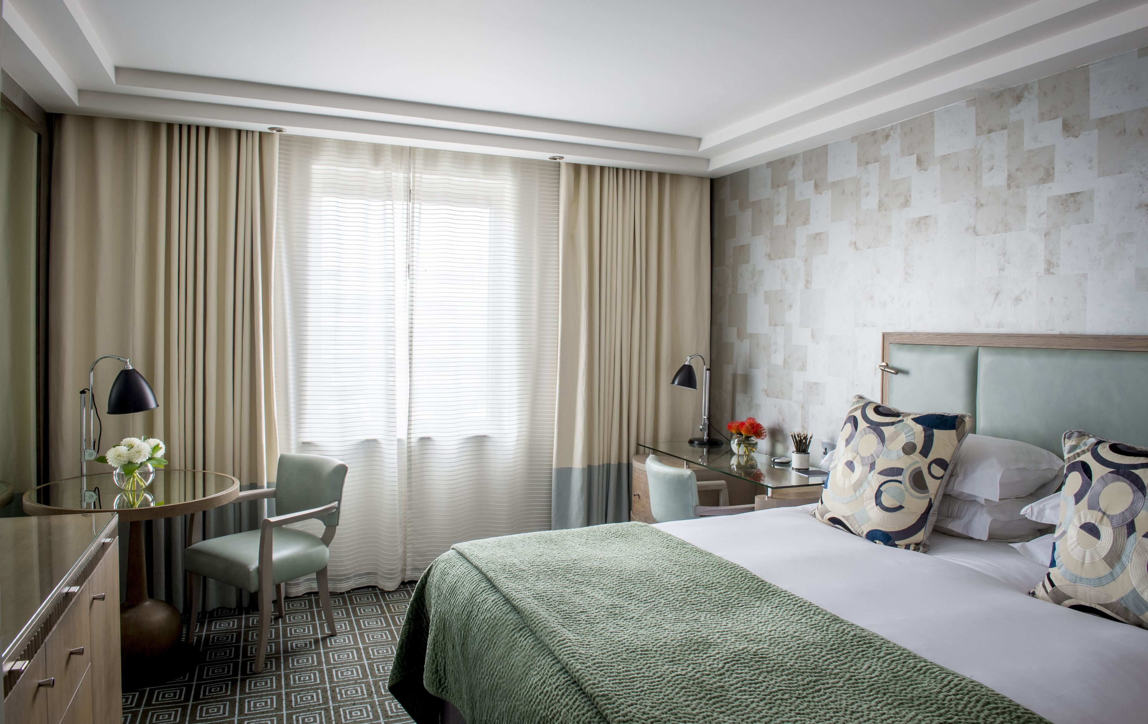Een hotelkamer met een bed, een bureau met lamp, een stoel en een raam met gordijnen.