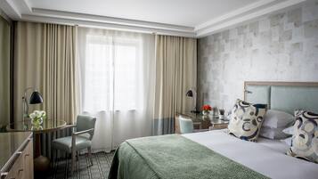 Een hotelkamer met een bed, een bureau met lamp, een stoel en een raam met gordijnen.