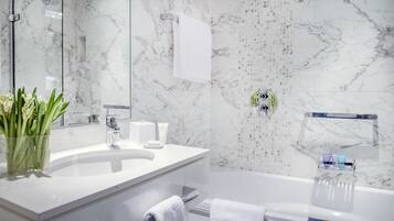 Une salle de bain moderne avec un lavabo en marbre, une cabine de douche en verre et une serviette blanche sur le sol.