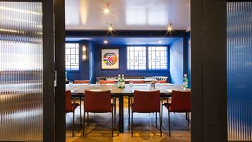 A modern dining area with a long table, red chairs, and a blue accent wall.