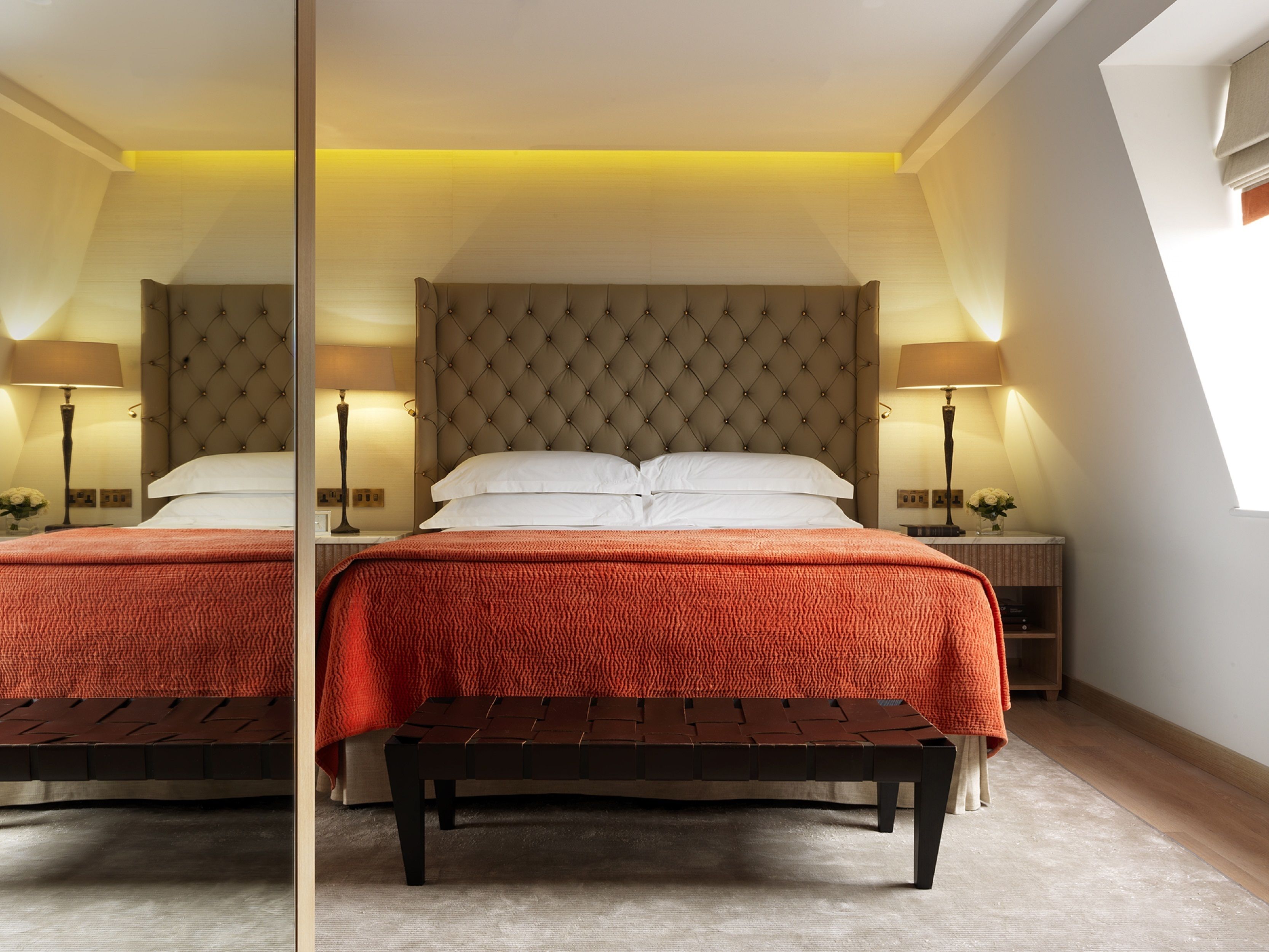 Une chambre d’hôtel avec un grand lit, deux tables de chevet, un banc et un plafond en pente doté de fenêtres de toit.