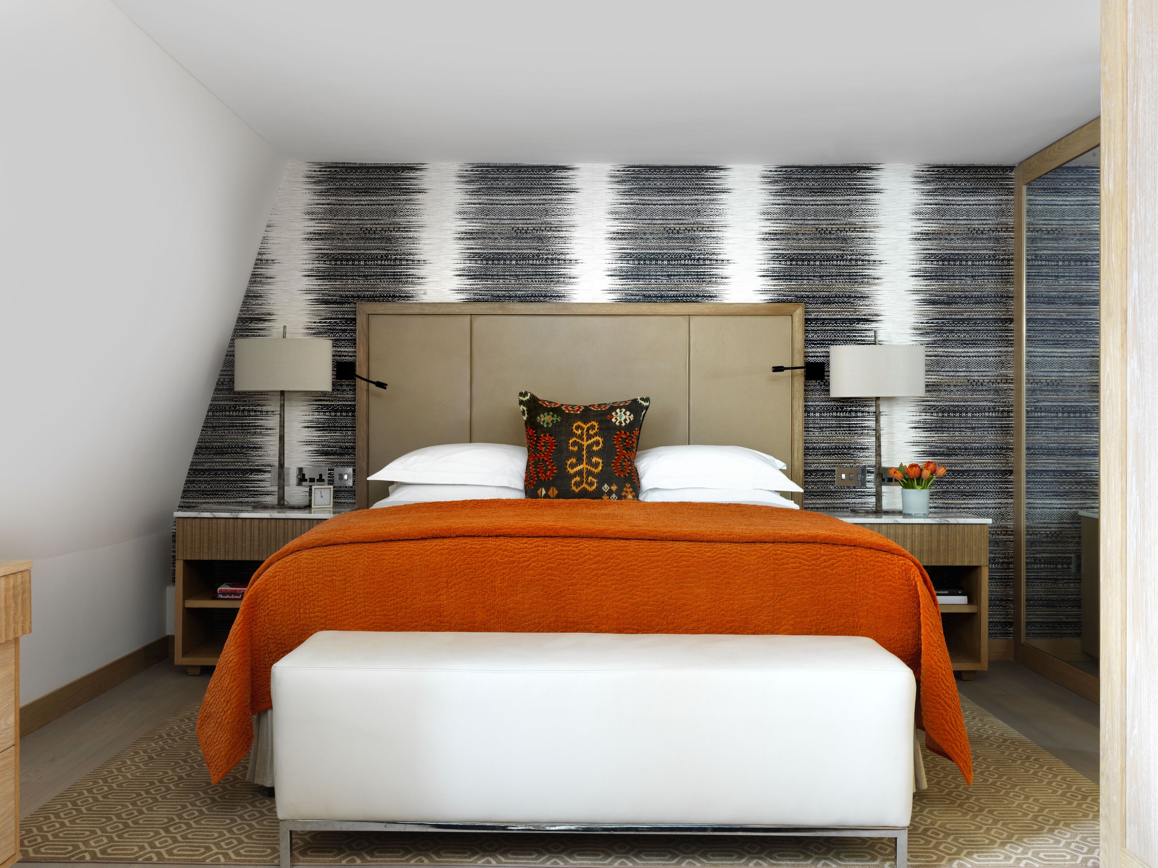 A modern hotel room with a large bed, a bedside table with a lamp, and a patterned wall.