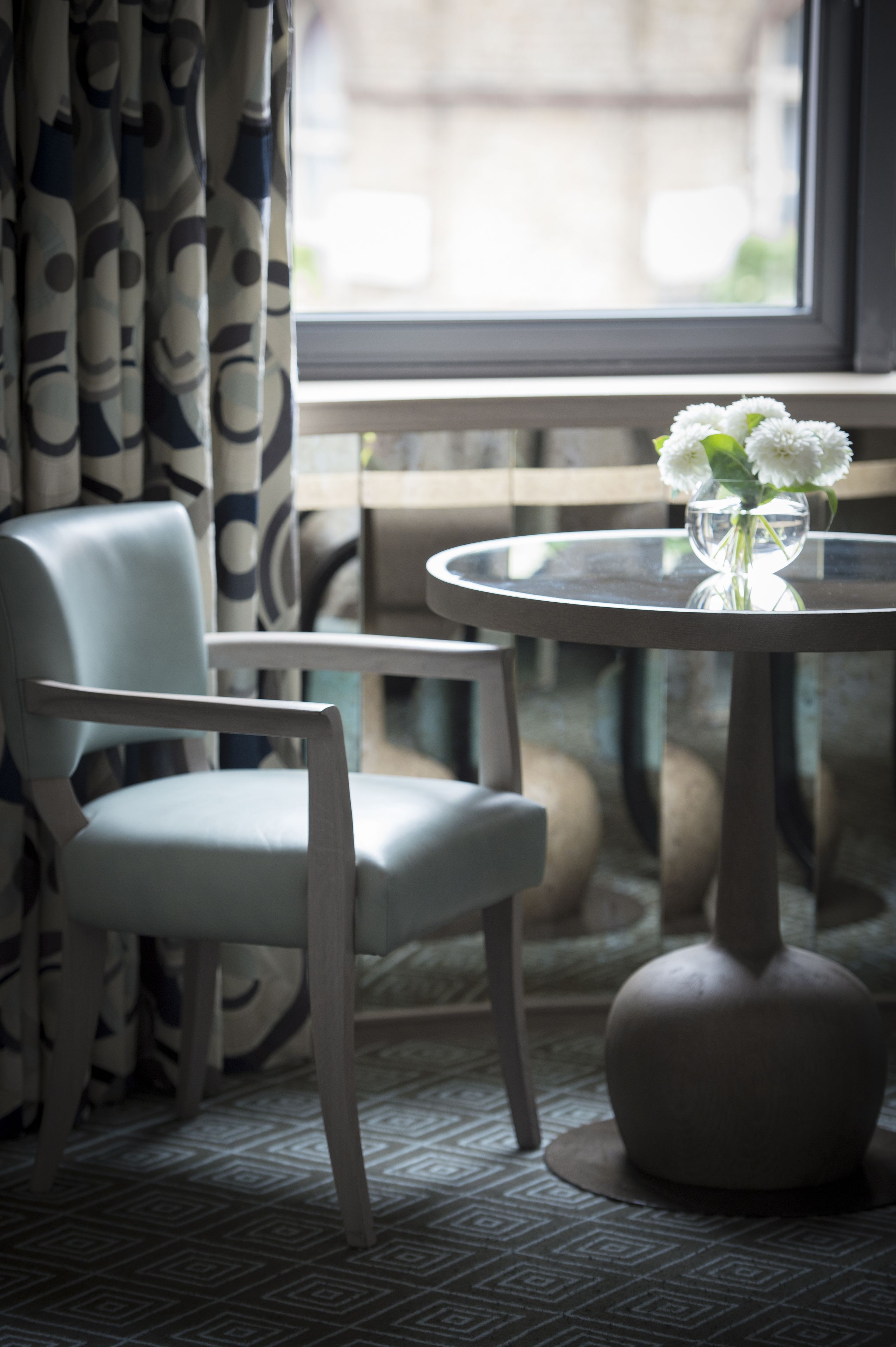 A room with a round table, a chair, and a vase with flowers.