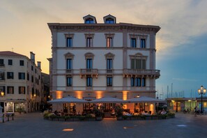 A historic building with multiple floors, large windows, and outdoor seating areas with umbrellas. - Hotel Grande Italia (Chioggia)