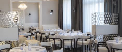 Un comedor formal con mesas redondas, sillas blancas y candelabros.
