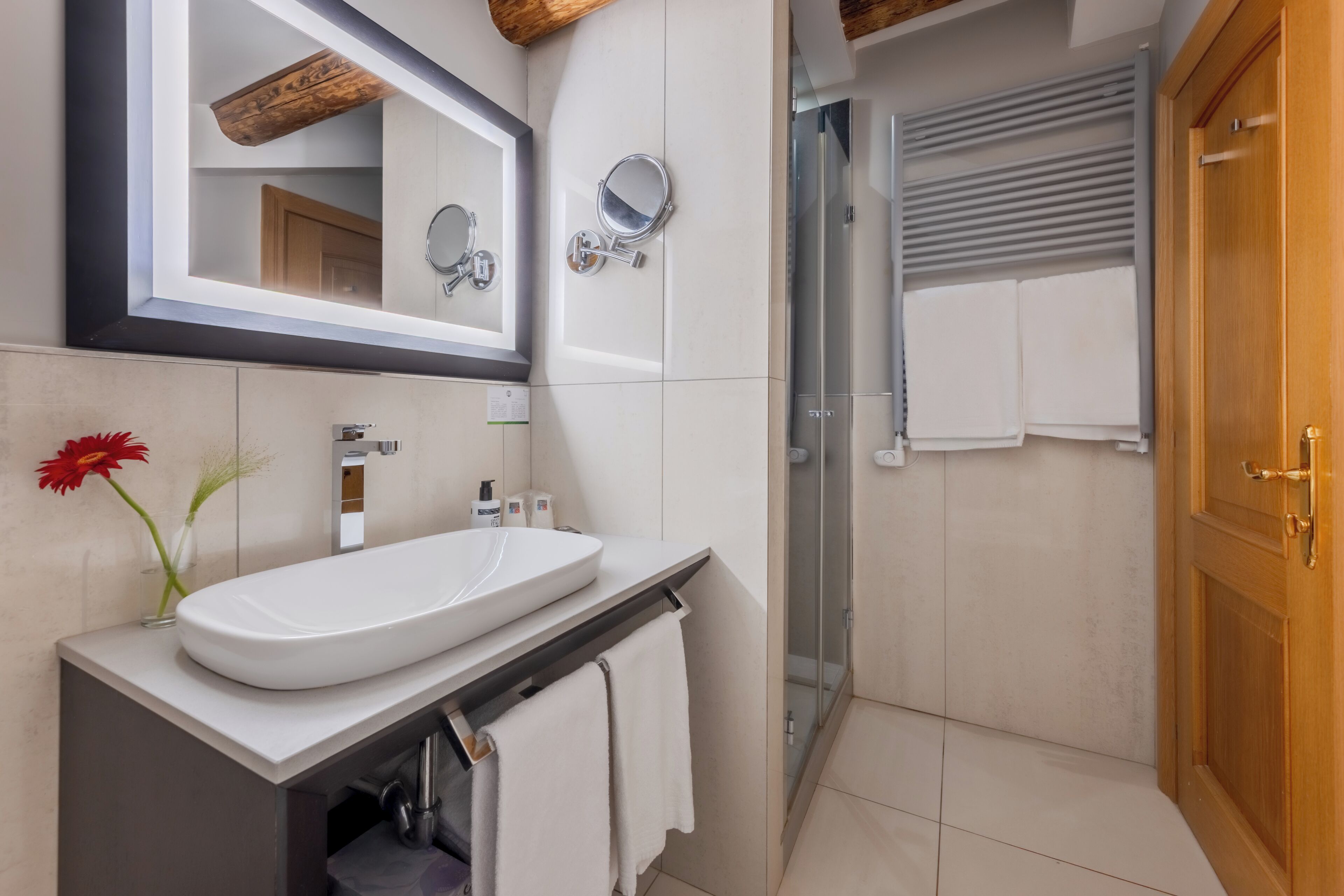 Une salle de bain moderne avec un lavabo blanc, deux miroirs, une douche et une porte en bois.