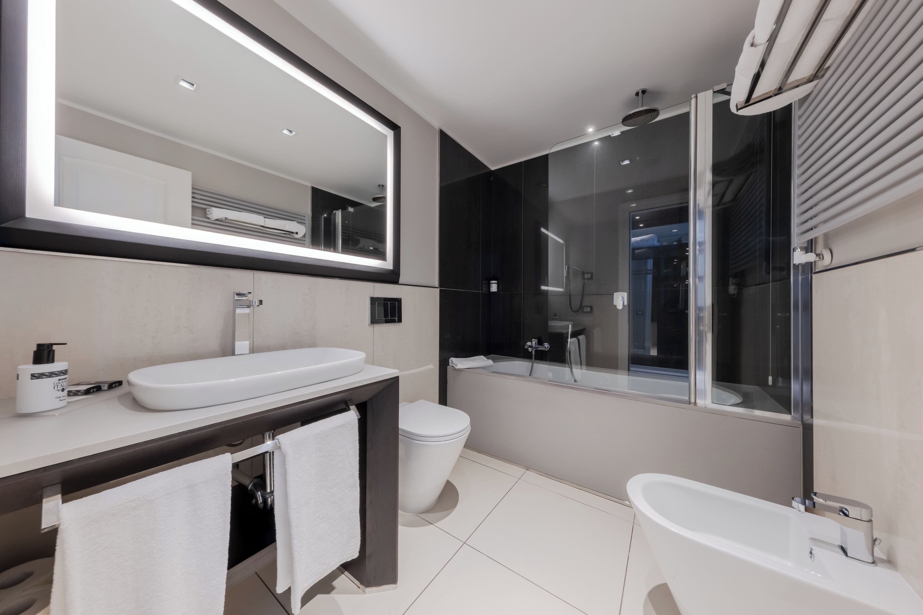 Un baño moderno con un espejo grande, un lavabo blanco, un inodoro y una bañera independiente.