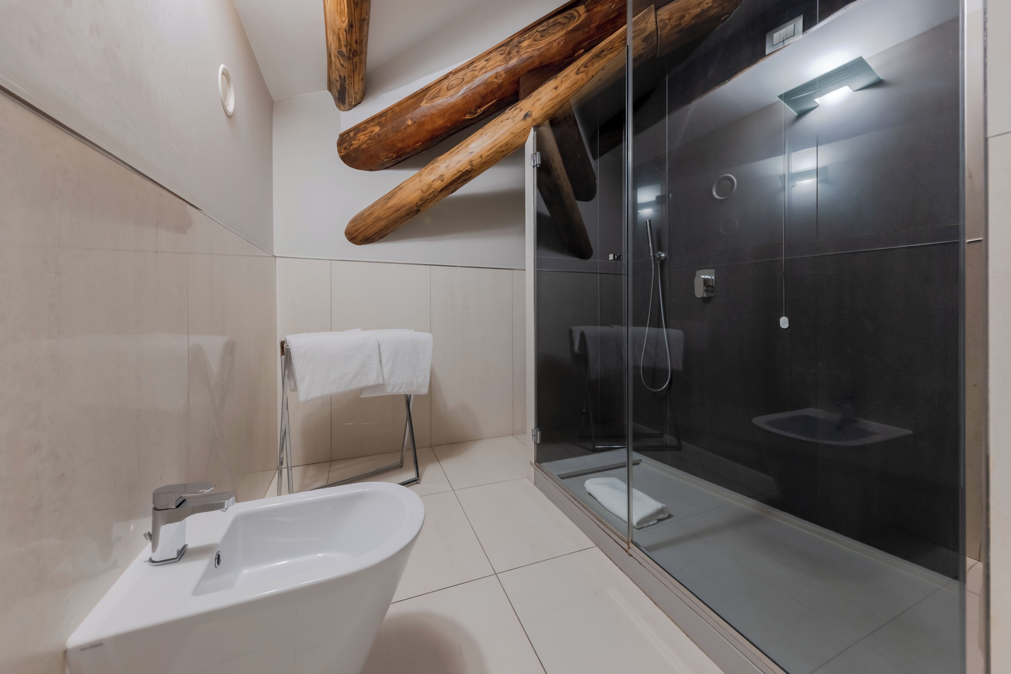 Un baño moderno con una bañera independiente, una ducha con cerramiento de vidrio y vigas de madera en el techo.