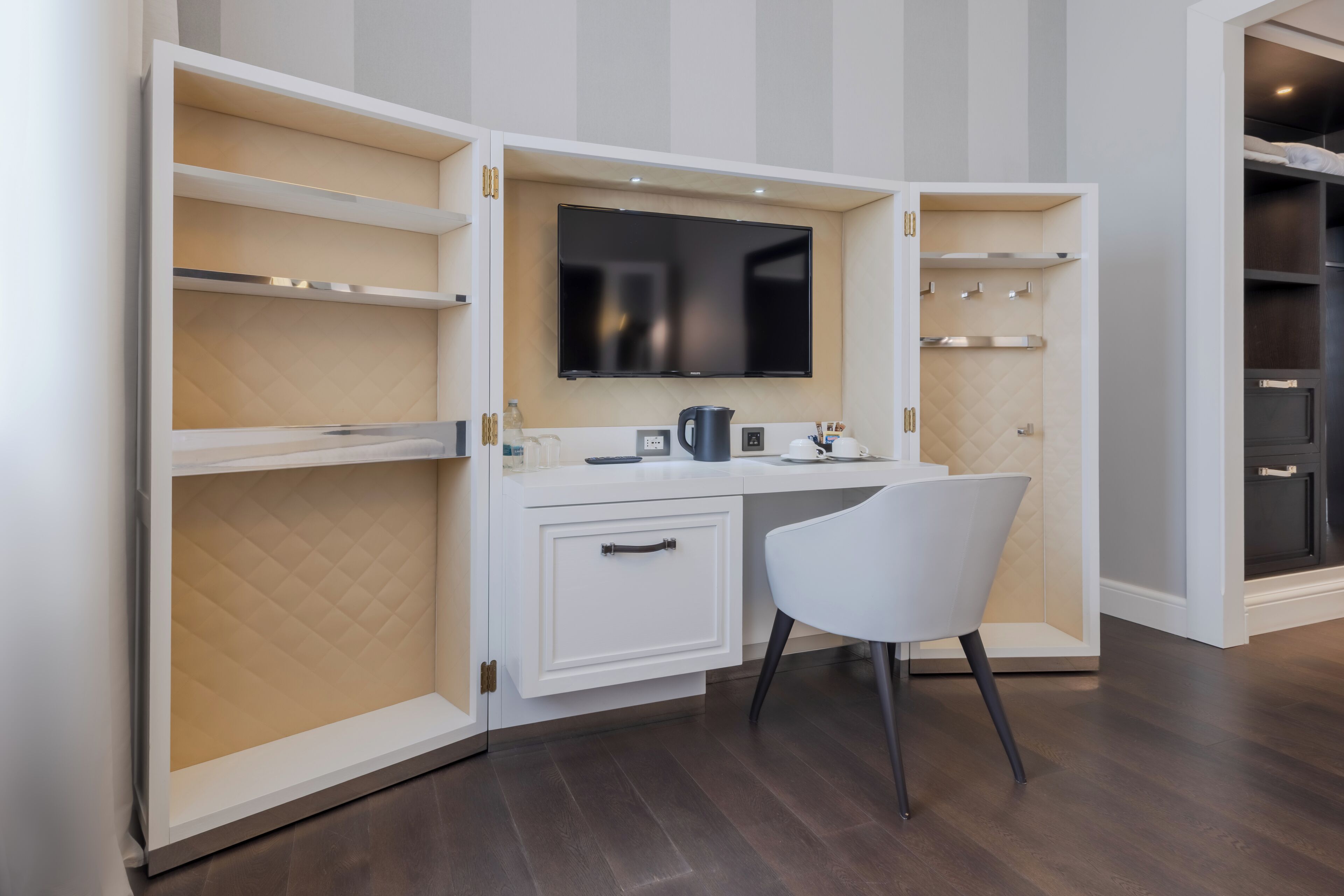 A modern kitchen with a built-in TV, white cabinetry, and a white chair.