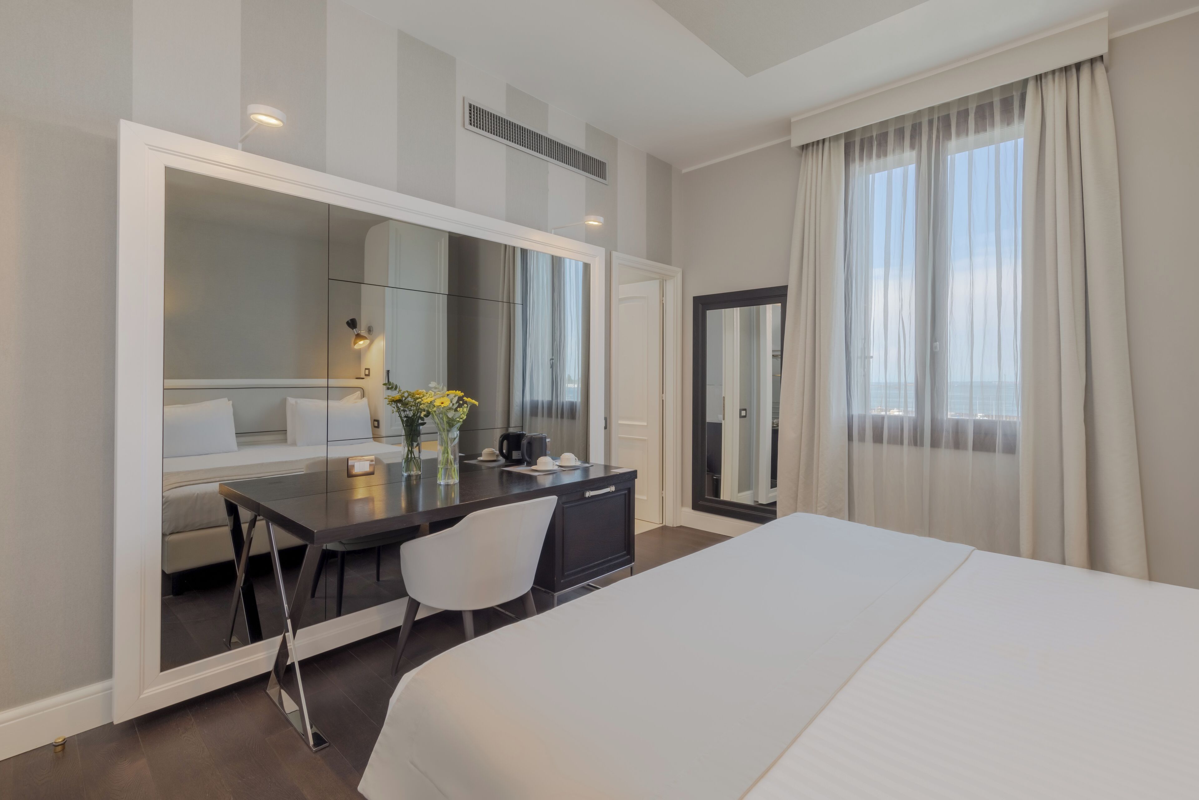 Een moderne hotelkamer met een groot bed, een bureau met stoel, een spiegel en uitzicht op de stad.