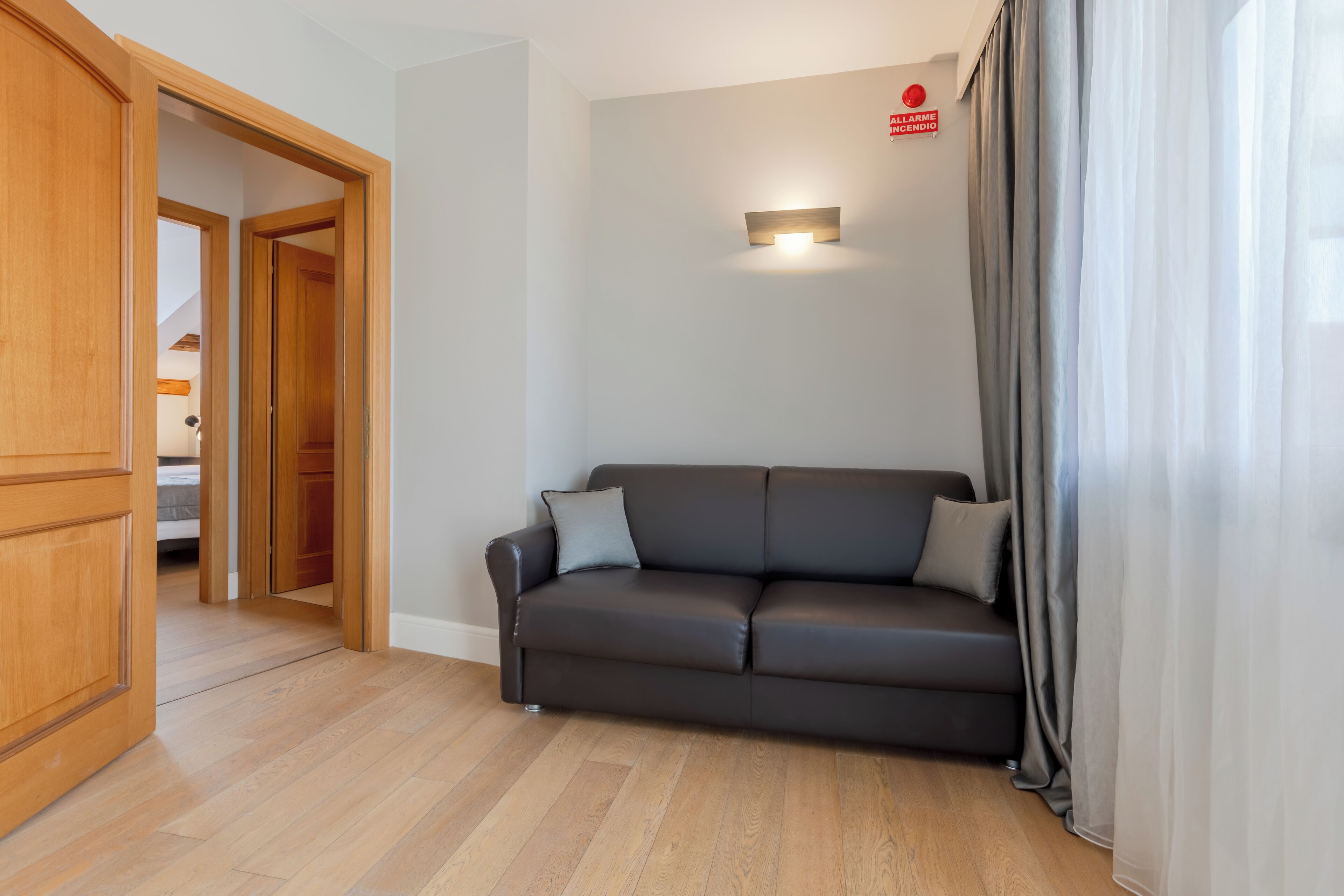 A modern living room with a dark leather sofa, wooden flooring, and a visible door leading to another room.