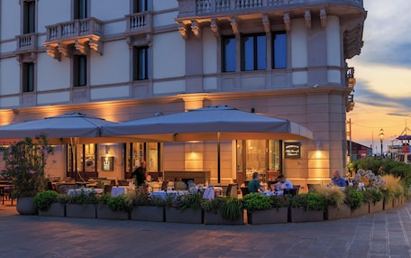 An outdoor dining area with tables and umbrellas, surrounded by planters with greenery.