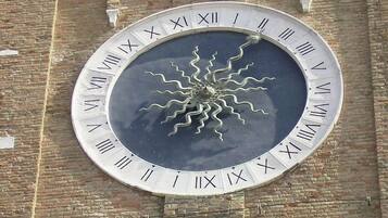 A large circular clock with Roman numerals against a brick wall.