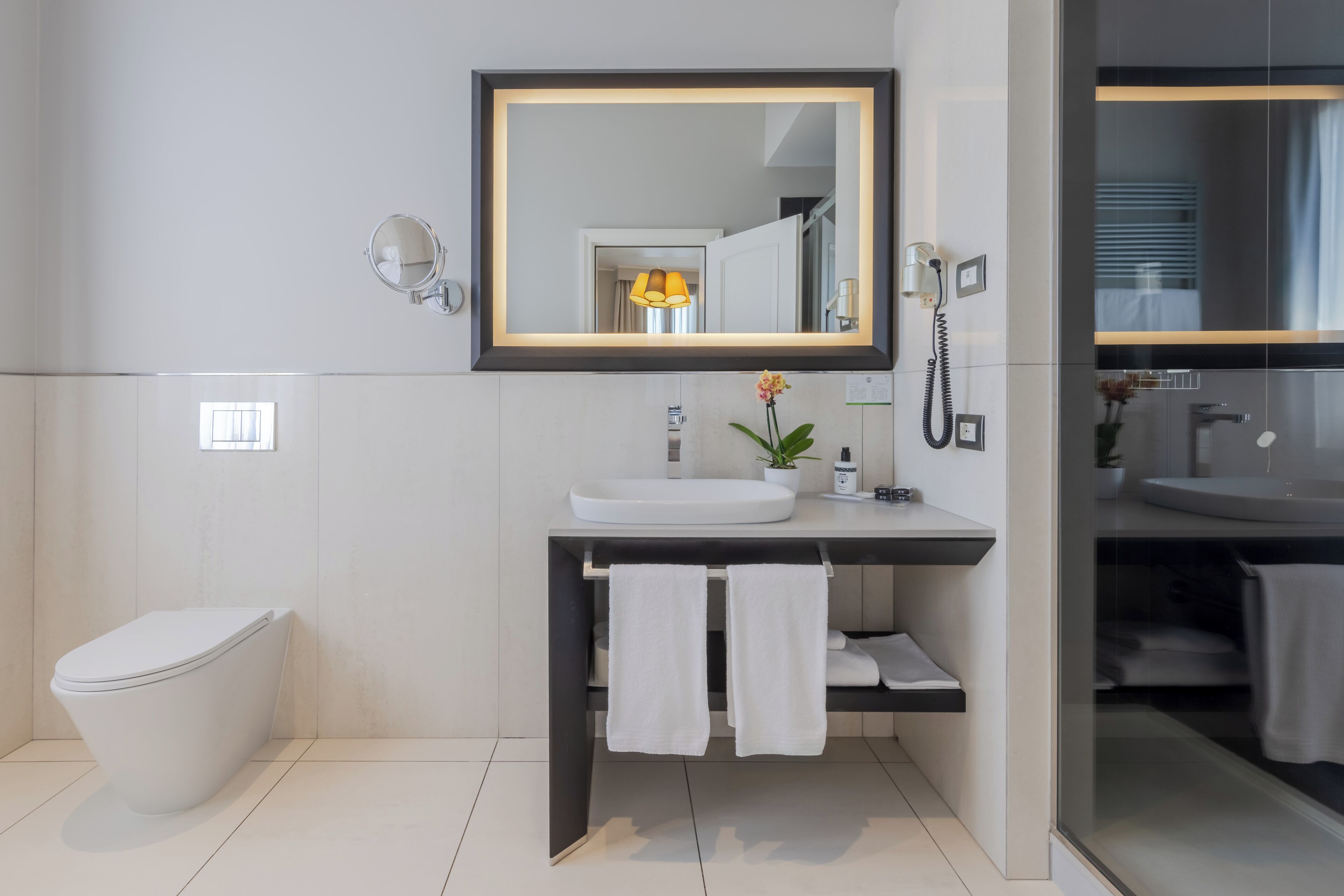 Een moderne badkamer met een wit toilet, een grote spiegel, een wastafel en een telefoon.