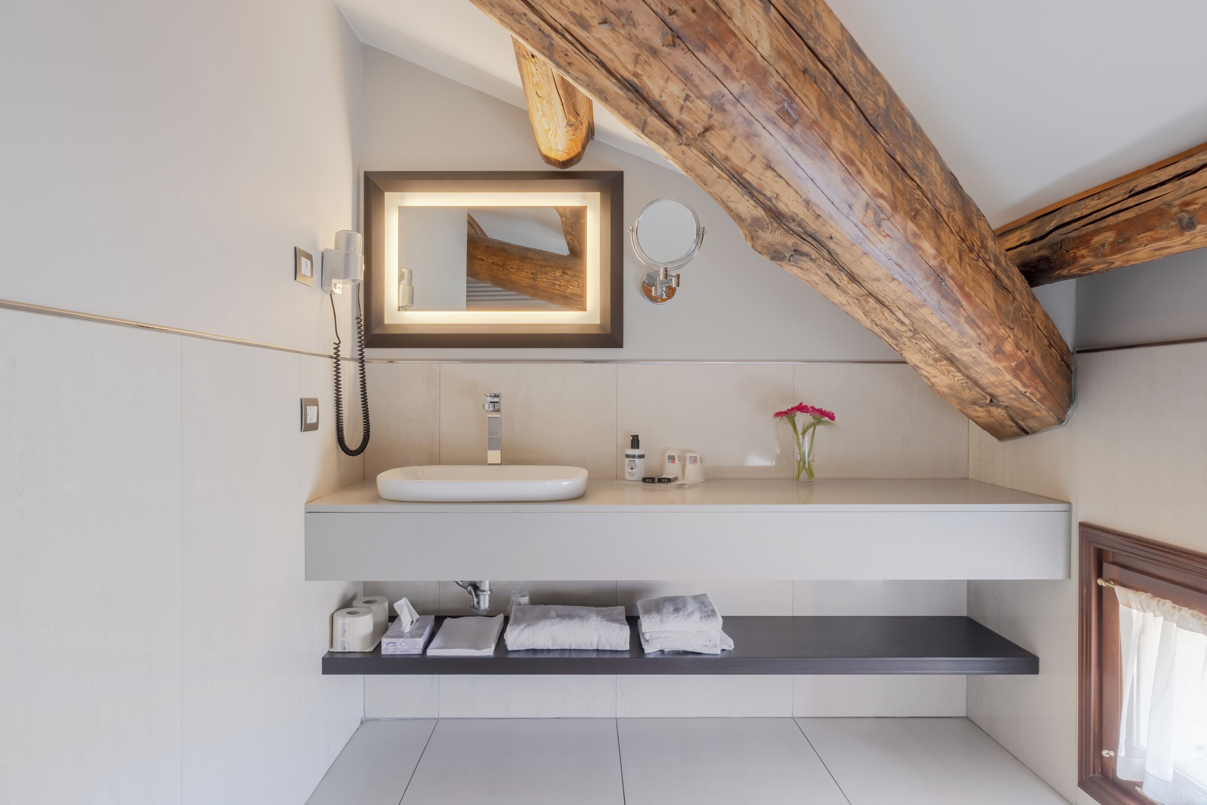 A modern bathroom with a large mirror, a built-in sink, and a wooden ceiling beam.