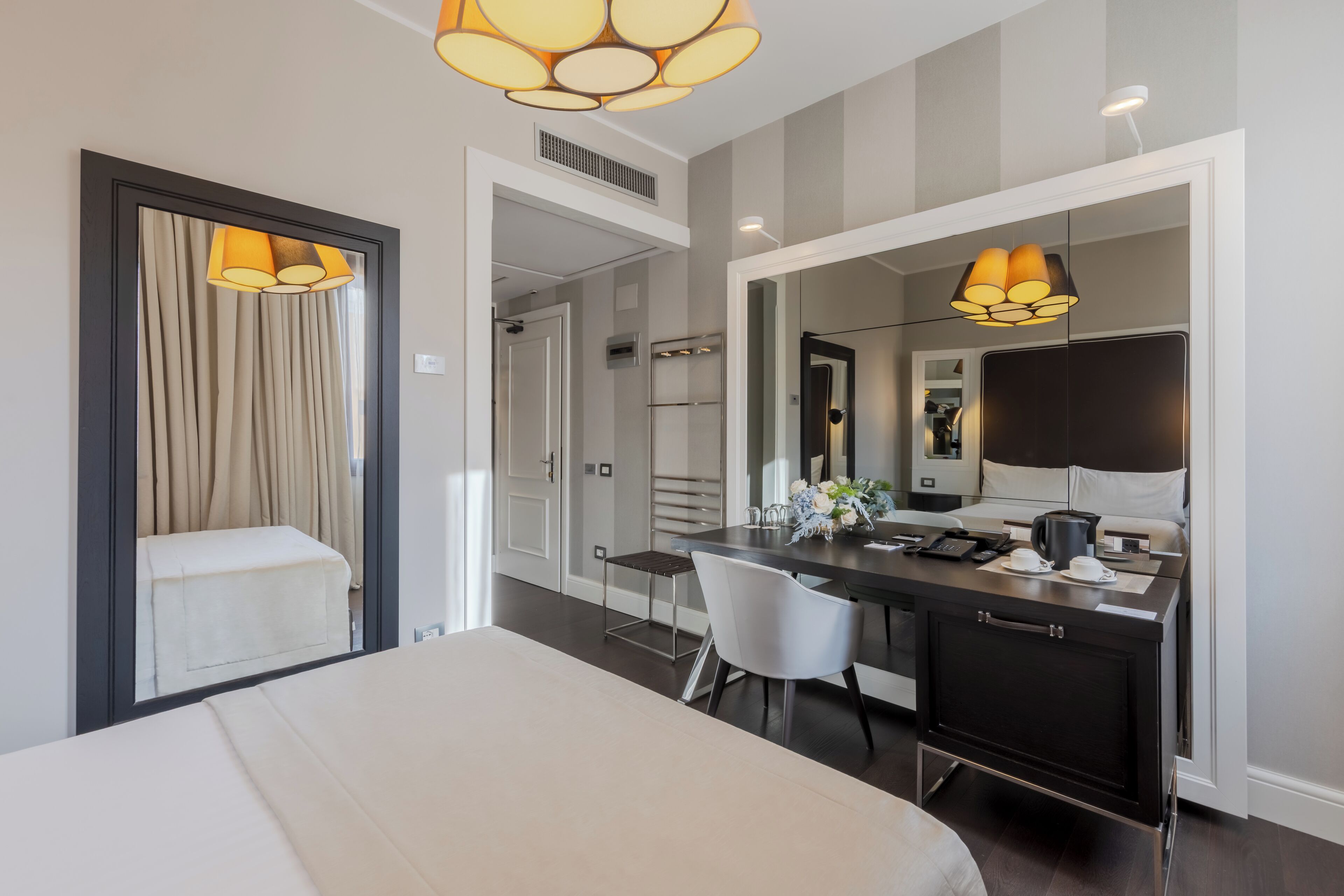 A modern hotel room with a large bed, a desk with a chair, a mirror, and two pendant lights.