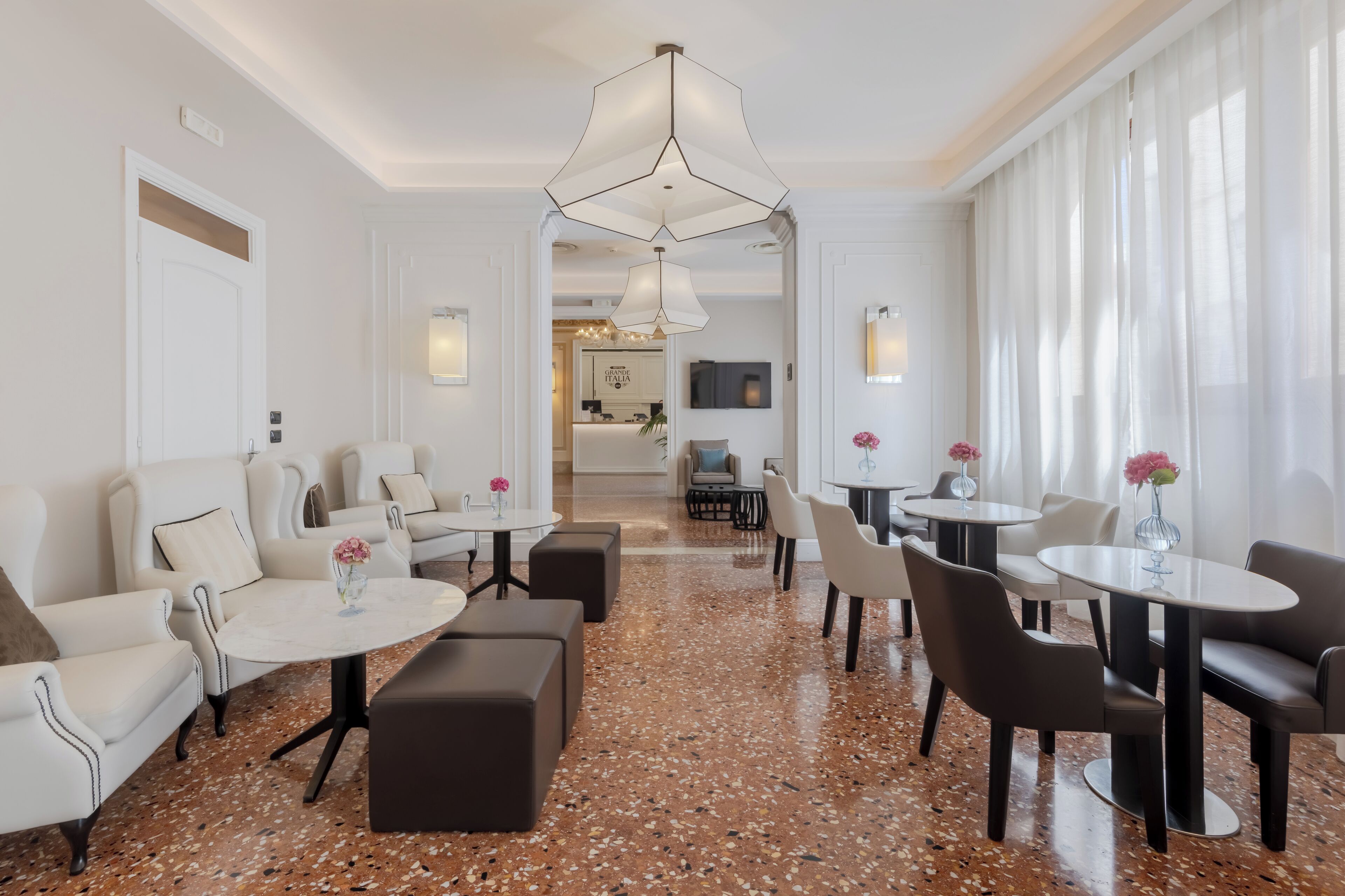 Eine moderne Hotellobby mit weißen Wänden, einem gefleckten Boden und einer Auswahl an Sitzmöglichkeiten, darunter Sofas und Tische.