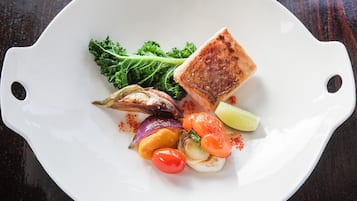 Une assiette blanche contenant divers aliments, notamment un morceau de viande grillée, des légumes et une tranche de citron vert.