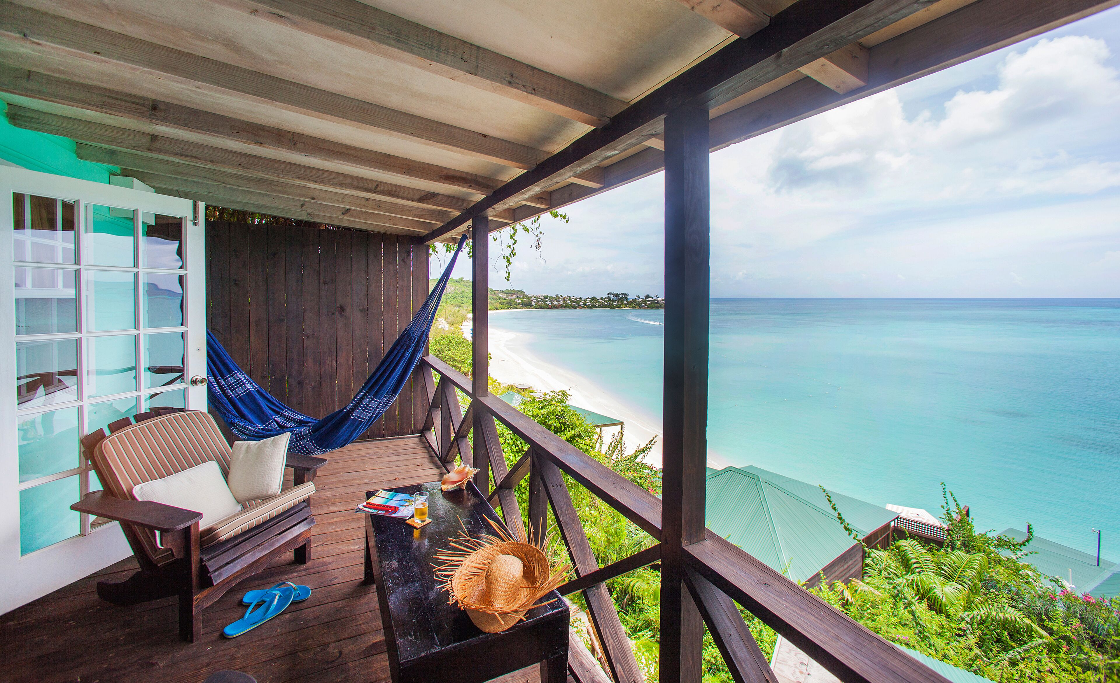 A wooden deck with a hammock, a chair, and a table with a straw hat and flip-flops.