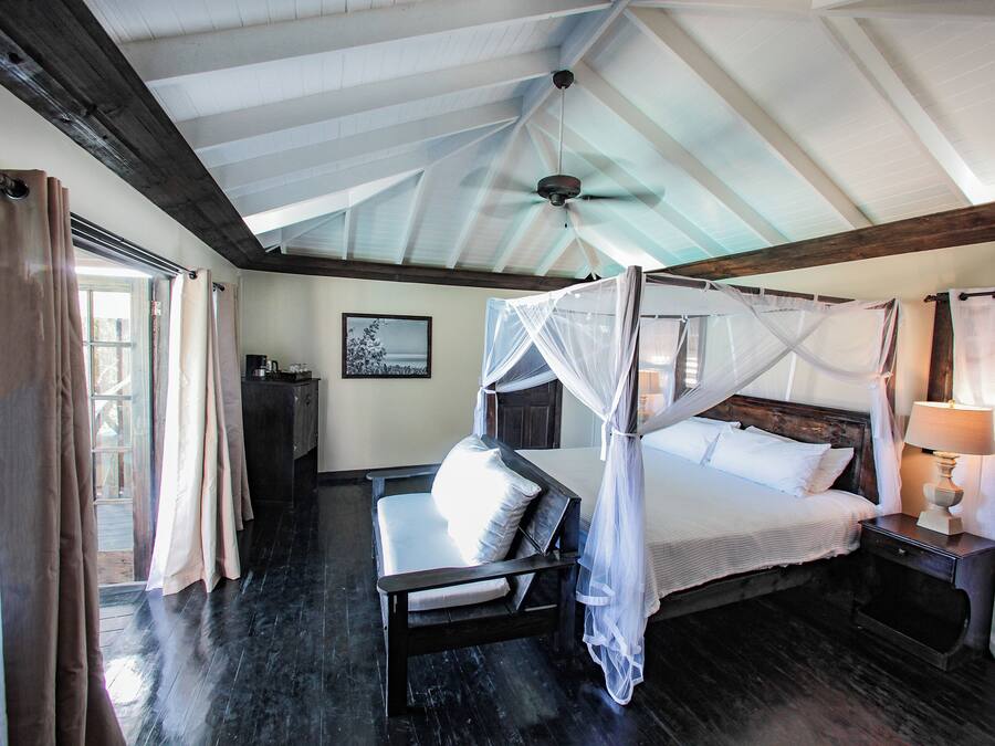 A bedroom with a four-poster bed, a bedside table with a lamp, and a wooden bench.