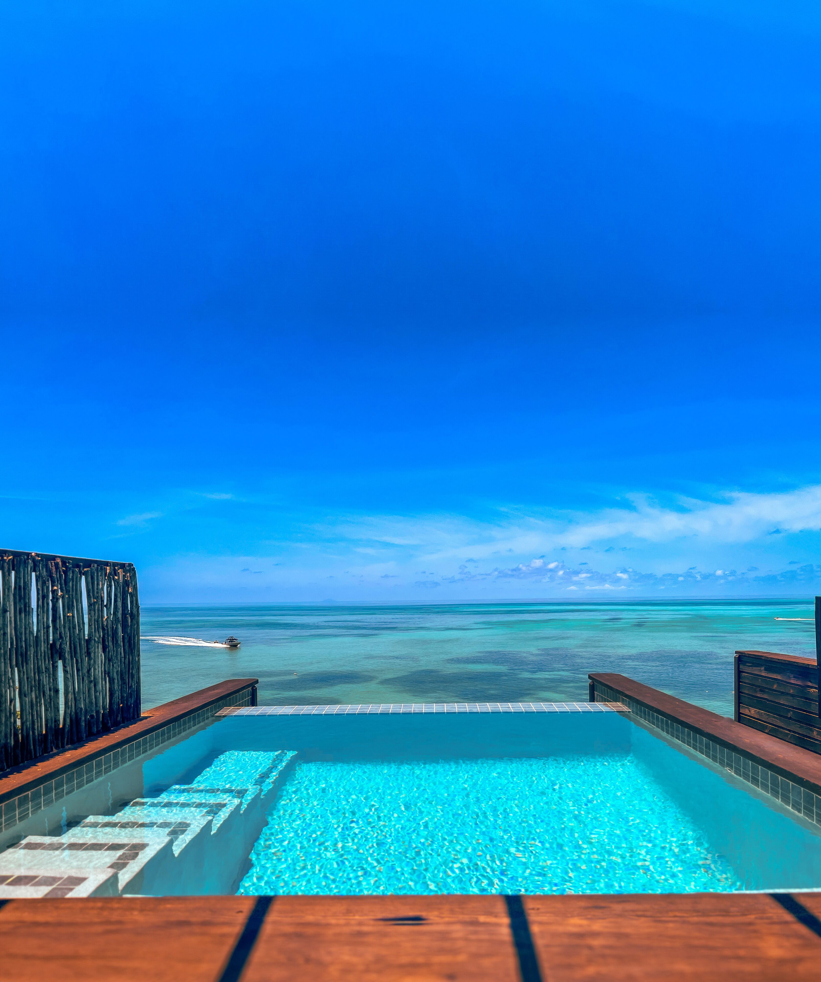 An infinity pool with a clear view of the ocean and a wooden deck.