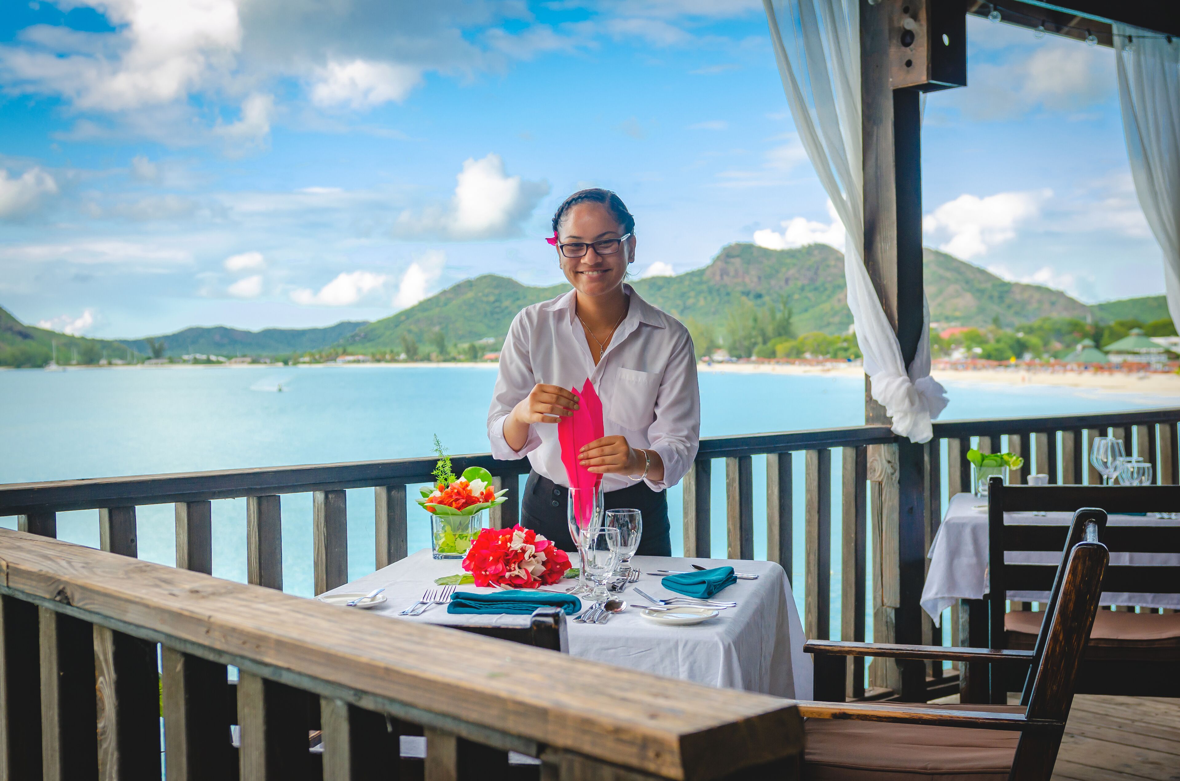 A dining area with a table set for two, overlooking a body of water and a beach.
