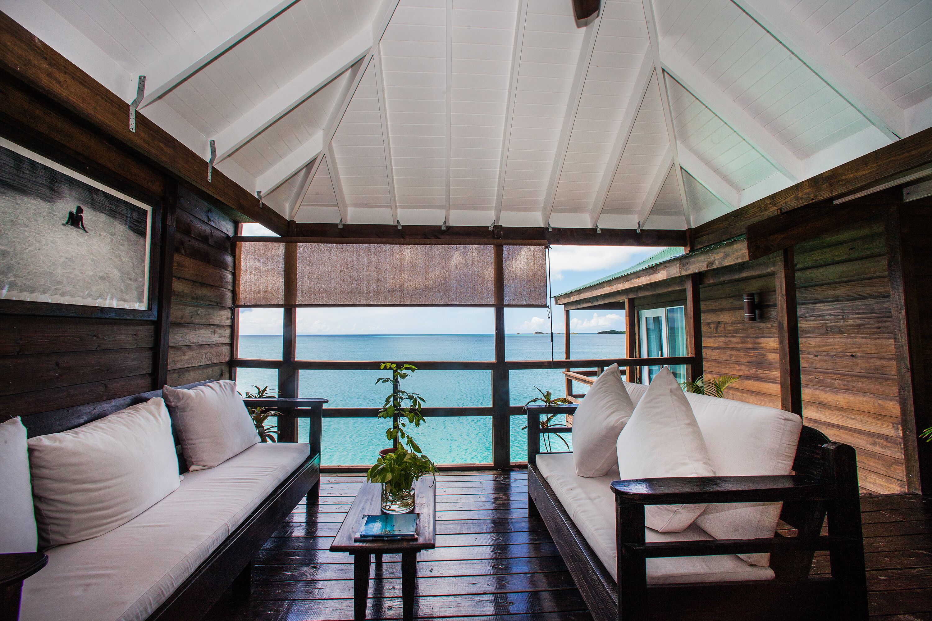 A wooden deck with a white sofa and a small table, overlooking a body of water.
