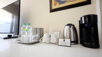 Habitación de hotel con escritorio, dos botellas de agua, cafetera, tetera y un cuadro en la pared.