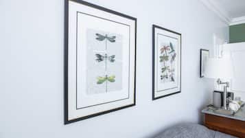 Una habitación con dos láminas botánicas enmarcadas en la pared, una lámpara sobre una mesita auxiliar y un sofá gris.