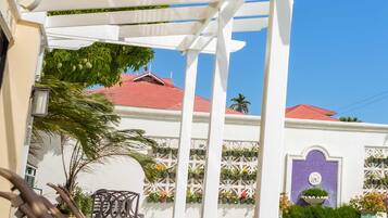 A poolside area with lounge chairs, a pergola, and a building with a red roof and decorative wall.