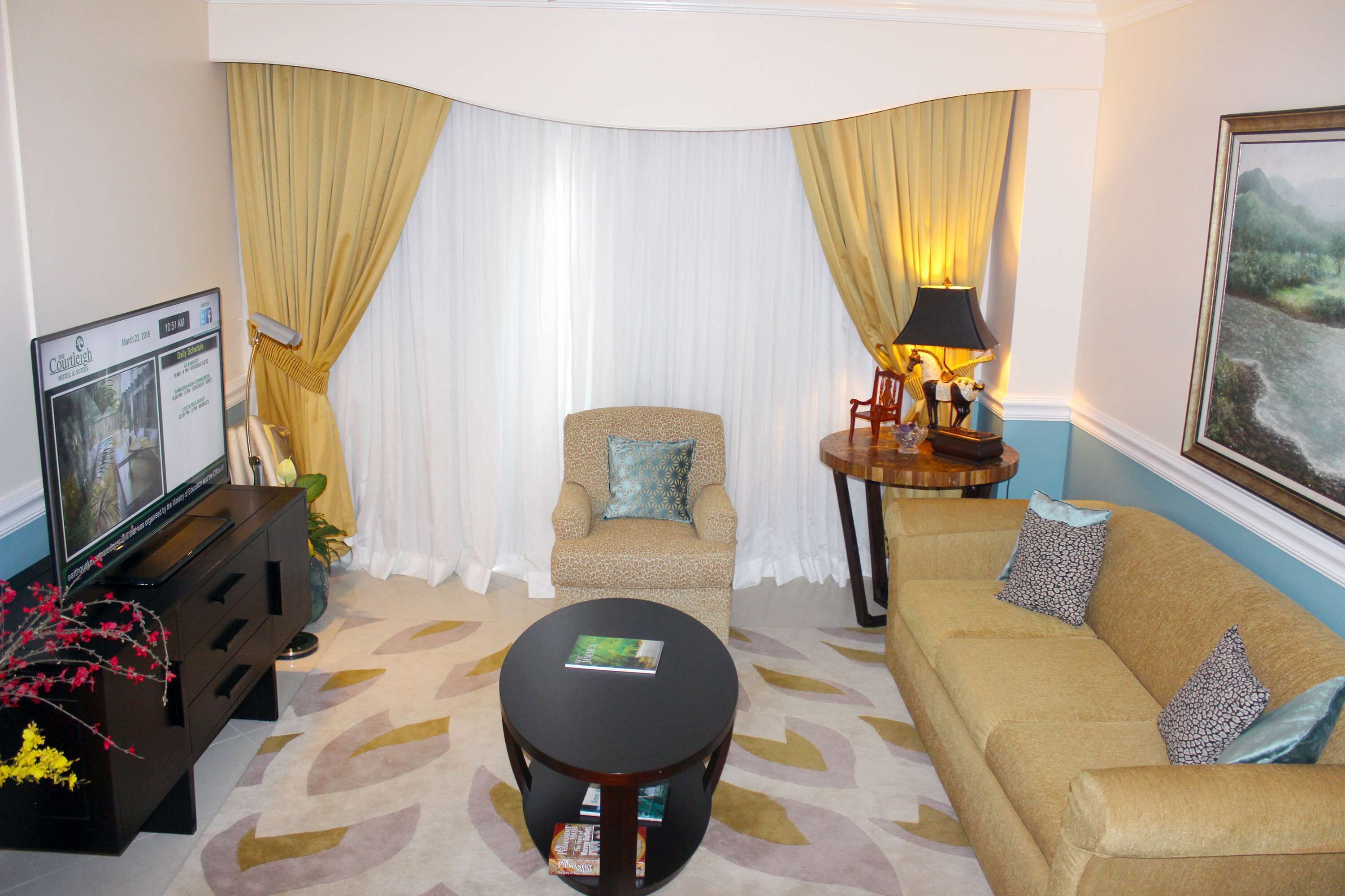 A living room with a sofa, armchair, coffee table, TV, and curtains.