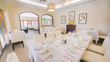 A dining area with multiple tables set for a formal event, featuring white tablecloths, chairs, and neatly arranged tableware.