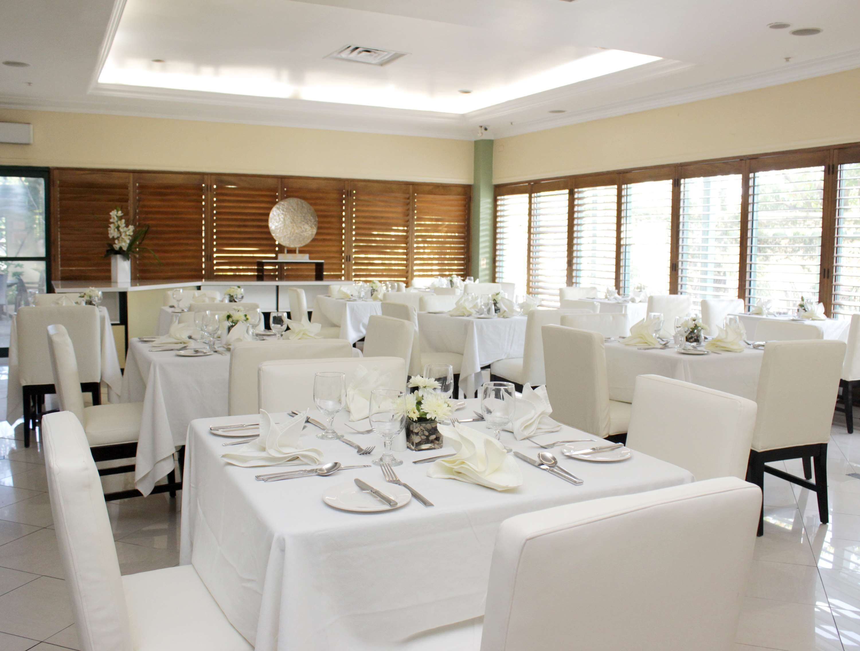 Un comedor amplio con varias mesas dispuestas para un evento formal, con manteles blancos y sillas.