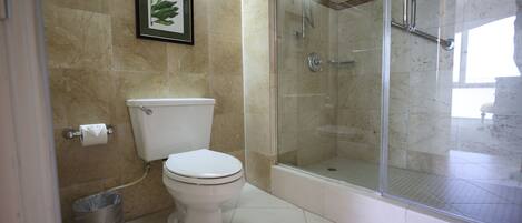 A bathroom with a toilet, a glass-enclosed shower, and a marble floor.