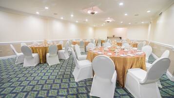 Un salón de conferencias con mesas redondas, sillas blancas y una alfombra estampada.