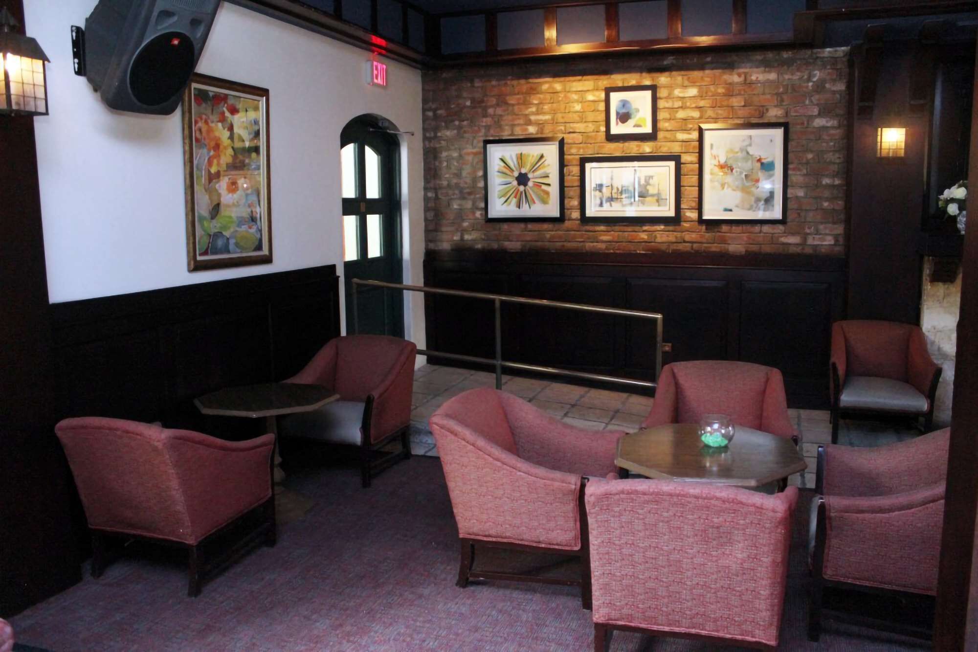 A cozy interior with red upholstered chairs, a small table, and a brick wall adorned with framed artwork.