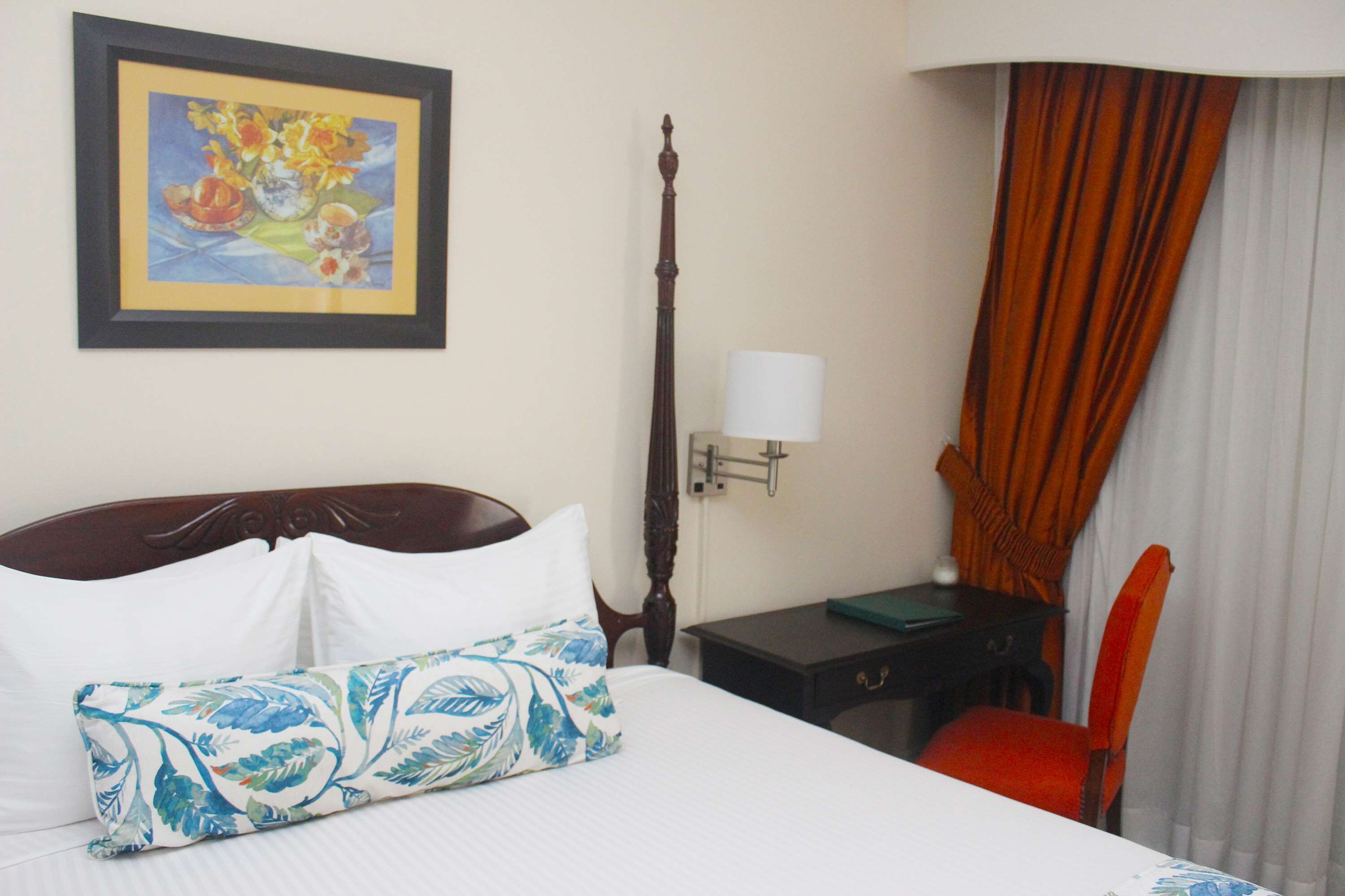 Habitación de hotel con cama, mesita de noche, lámpara, sillón y un cuadro en la pared.
