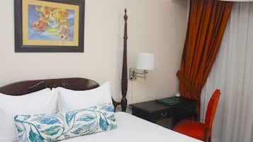 Habitación de hotel con cama, mesita de noche, lámpara, sillón y un cuadro en la pared.