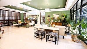 A spacious lobby with a high ceiling, a central seating area with a table and chairs, and a large window providing natural light. - The Courtleigh Hotel and Suites (Kingston)