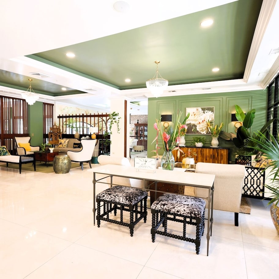 A spacious lobby with a high ceiling, a central seating area with a table and chairs, and a large window providing natural light.
