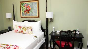 A hotel room with a bed, a desk, a chair, a lamp, a painting, and a trash can.