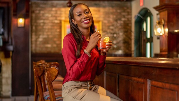A person seated at a wooden bar with a stone-tiled floor, holding a drink. - The Courtleigh Hotel and Suites (Kingston)