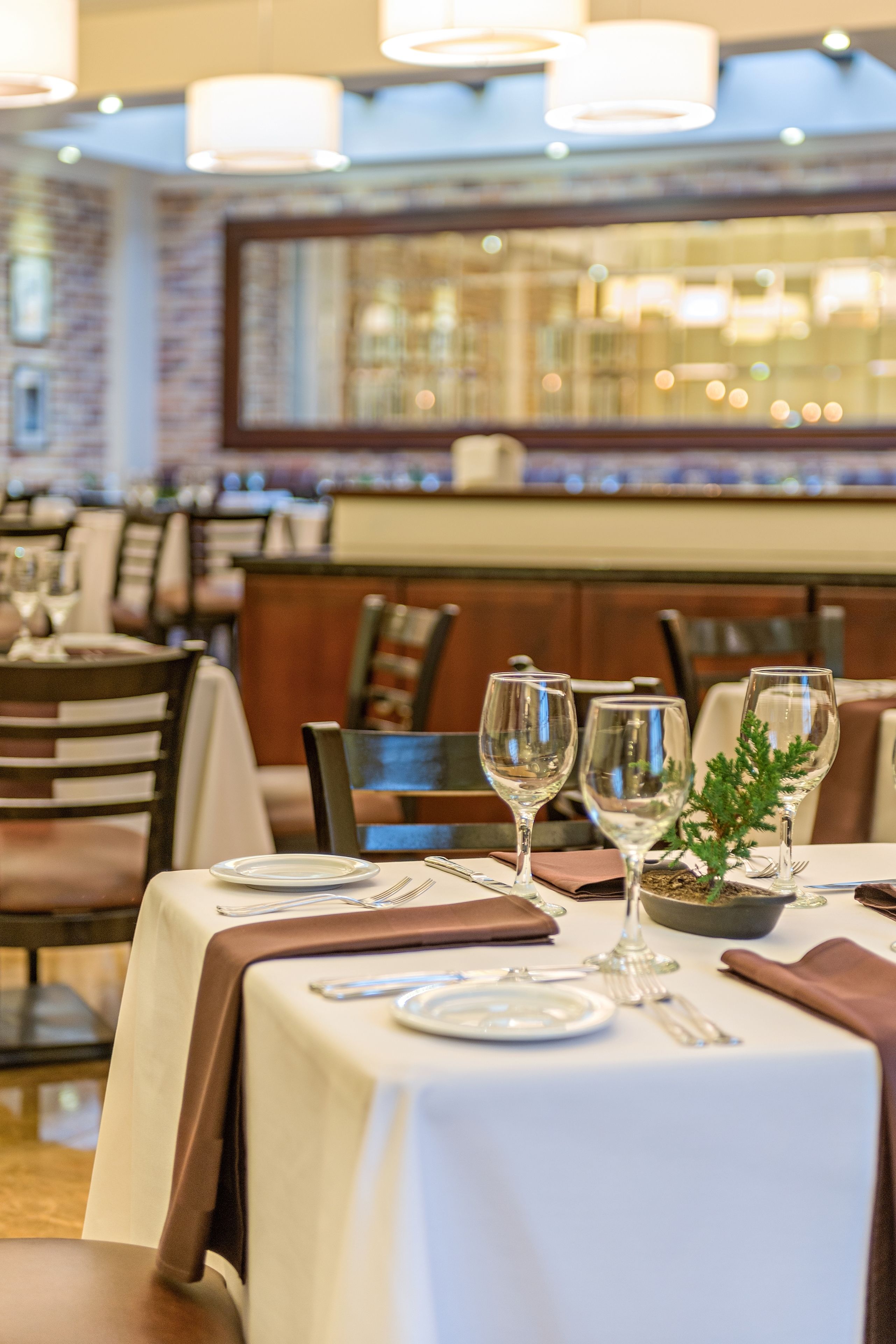 A restaurant with tables set for dining, featuring white tablecloths and brown napkins.