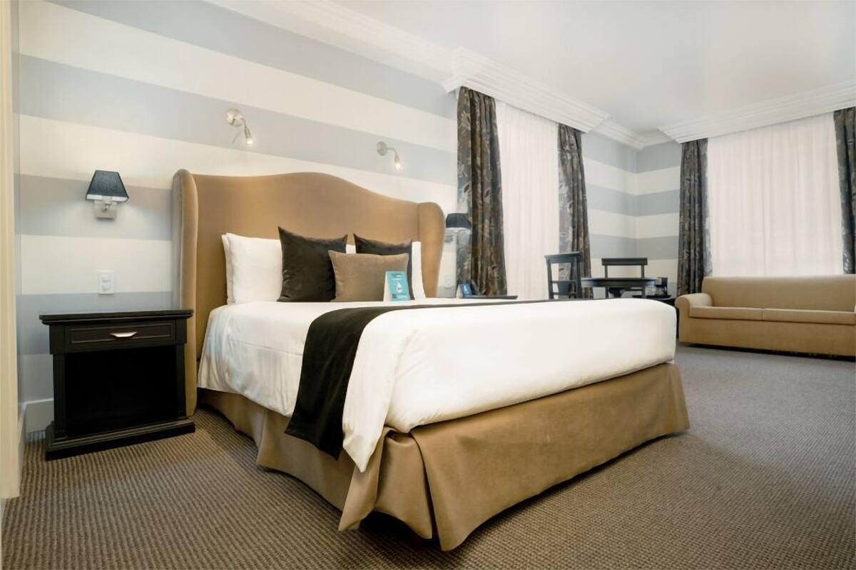 A hotel room with a large bed, a bedside table, a chair, and a sofa.