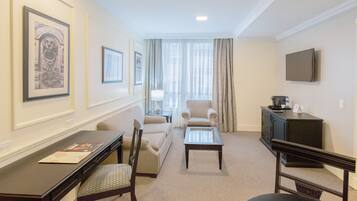 Habitación de hotel con sofá, sillón, mesa de centro, televisión y cuadros en las paredes.
